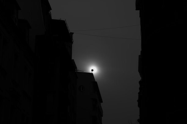 在黑暗的夜晚，碟形卫星覆盖了建筑物之间的月亮图片下载