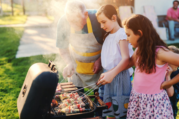 祖父教他的孙子们如何烧烤。家庭聚会在后院里的概念。图片下载