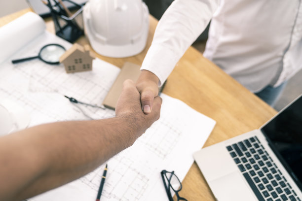 建筑师或土木工程师与客户或客户握手同意房屋或建筑平面图，平面图是伪造的，仅供库存照片。图片下载