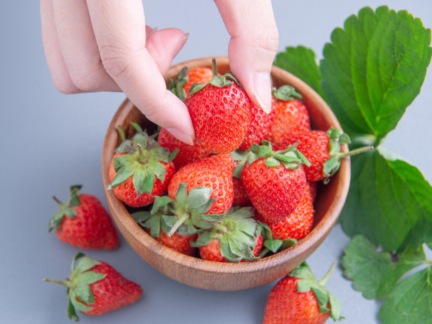 一个年轻的女人拿着一碗草莓，孤立在一个轻快的蓝色背景上，特写，topview, copyspace。图片下载