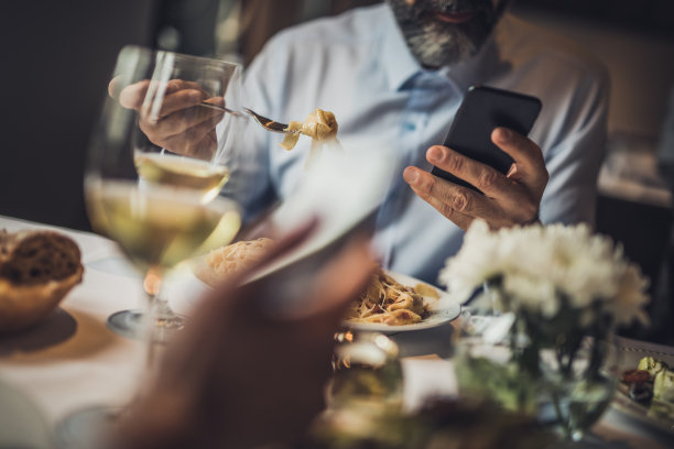 一个面目全非的人在餐厅吃午餐时用手机。图片下载