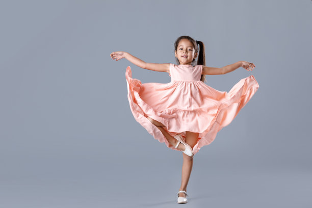穿着粉红色裙子的小女孩在灰色背景下摆姿势。图片下载