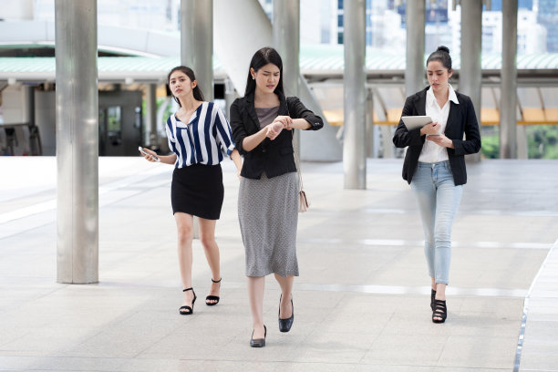 一群年轻的商业妇女在高峰时间走在街上，看着时钟检查时间到晚在城市街道上图片下载