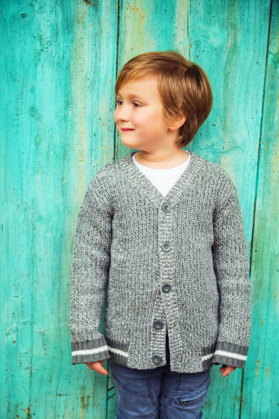 5-6岁男孩在户外摆姿势，穿着灰色针织羊毛衫，站在绿松石背景下图片下载