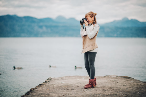 可爱的小女孩在日内瓦湖上享受美好的一天，穿着米色夹克，用单反相机拍照。有孩子的旅行。图片拍摄于洛桑;瑞士图片下载