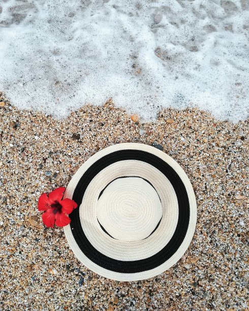 草帽躺在海边的沙滩上，花儿是红色的。夏天的观点。图片下载