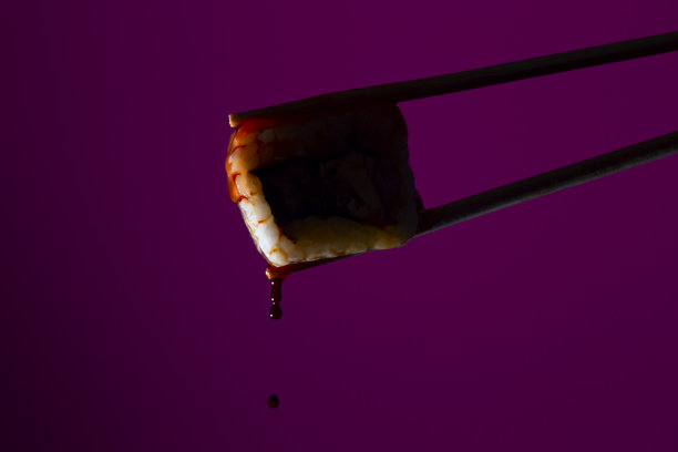在彩色的背景上，筷子之间的多汁卷的剪影，从寿司滴酱油，食物背景，日本料理图片下载