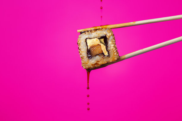 多汁的卷在筷子之间的彩色背景，酱油滴从寿司，食物的背景，日本料理图片下载