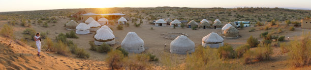 在乌兹别克斯坦红色Kyzykum沙漠的Aydar湖的边缘，一名老妇人在拍下太阳从蒙古包上升起的照片后看着相机图片下载