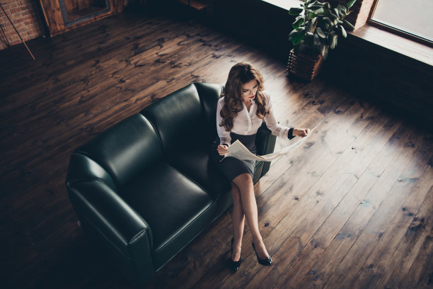 上面的高角度的好看可爱的时尚时髦时髦迷人的女士商业鲨鱼坐在沙发上阅读晨报例行的工作地点站阁楼内部图片下载