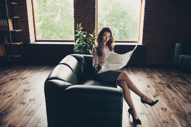 侧面的她，她漂亮，时髦，优雅，奢侈，有吸引力，迷人的卷发女士坐在沙发上读晨报，长腿，裙子，工作地点，站阁楼内部图片下载