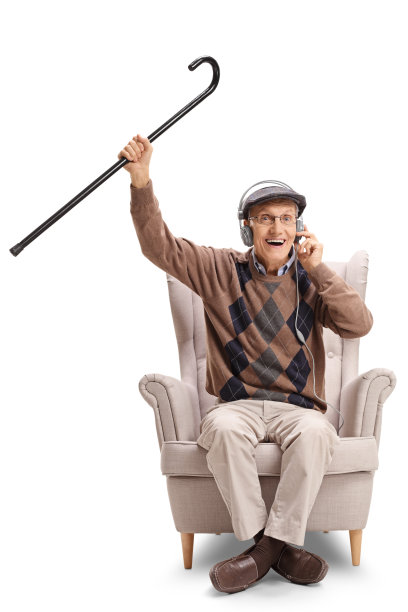 快乐的老人坐在扶手椅上，戴着耳机听音乐，拄着拐杖图片下载