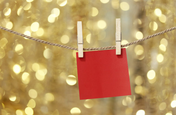 在散景灯的背景下，为圣诞节设计而挂在晾衣绳上的空白红纸纸条。图片下载