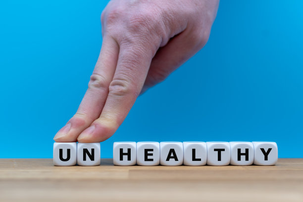 骰子组成单词“不健康”，而两个手指推开字母“UN”，以改变单词“健康”。图片下载