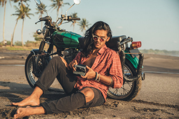 一名男子坐在海滩上的自行车旁，手里拿着即时照相机图片下载