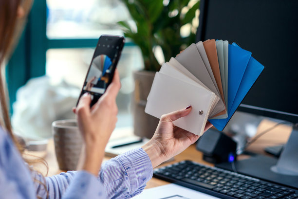 女设计师在办公室工作与颜色样品。职场女性用智能手机拍调色板照片。图片下载