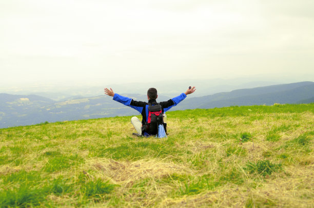 盖伊坐在山上的草地上，张开双手。图片下载