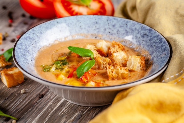 西班牙菜的概念。新鲜西红柿做成的西班牙凉菜汤。在一家餐馆的木桌上，漂亮的上菜盘子装在一个蓝色的盘子里。的背景图片。本空间图片下载