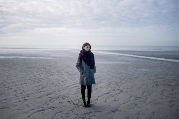 穿着大衣的年轻女子站在冬天的海滩上图片下载