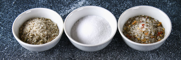 深灰色的桌子上放着玻璃碗，里面装着不同种类的盐。图片下载