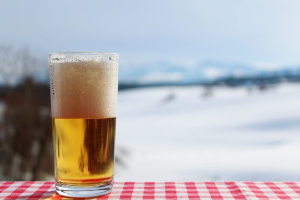 新酿的泡沫啤酒盖在菱形桌布上令人梦寐以求的坐落于山背景的冬景阿尔高，巴伐利亚图片下载