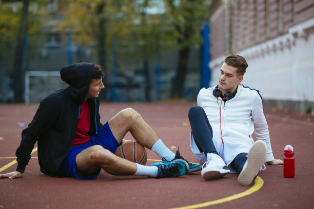 年轻的篮球运动员在比赛后坐在球场上休息图片下载