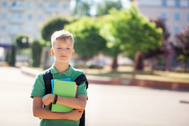 在阳光明媚的日子里，可爱的男孩在户外。拿着书包拿着书的少年图片下载