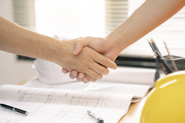 建筑师或土木工程师与客户或客户握手同意房屋或建筑平面图，平面图是伪造的，仅供库存照片。图片下载