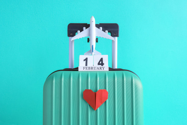 行李与情人节日期日历和飞机与纸心蓝绿色背景的简约度假概念。图片下载