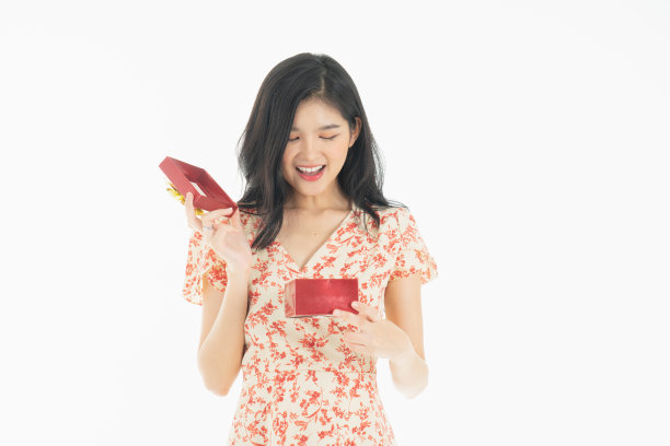 亚洲好奇的女人在红色裙子庆祝她的生日或新年礼盒的照片。年轻女子拿着礼盒与红色的蝴蝶结正在兴奋和惊讶的节日现在孤立的白色背景图片下载