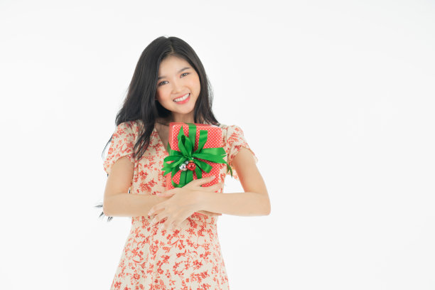 亚洲好奇的女人在红色裙子庆祝她的生日或新年礼盒的照片。年轻女子拿着礼盒与红色的蝴蝶结正在兴奋和惊讶的节日现在孤立的白色背景图片下载
