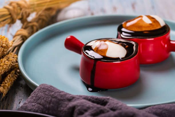 两个有把手的红色小杯子的横放照片。杯子里装满了香甜的生奶油。液态黑巧克力在奶油上面，顺着杯子流淌。杯子在蓝色的盘子里。图片下载