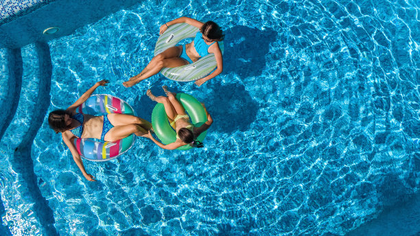 家庭在游泳池空中无人机从上面看，快乐的母亲和孩子游泳在充气圈甜甜圈和有乐趣的家庭度假，热带度假度假胜地图片下载
