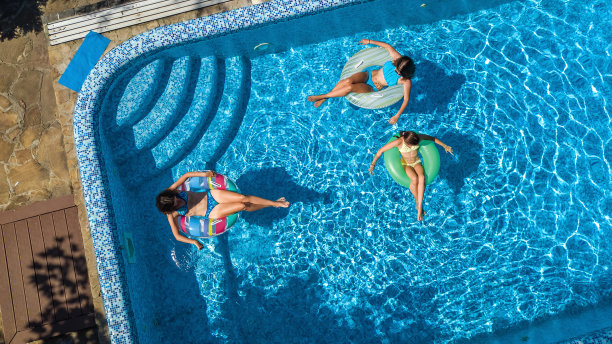 家庭在游泳池空中无人机从上面看，快乐的母亲和孩子游泳在充气圈甜甜圈和有乐趣的家庭度假，热带度假度假胜地图片下载