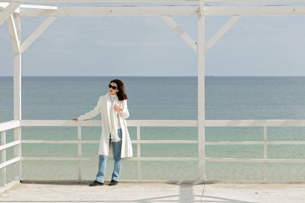 一位身穿白大褂的年轻女子(褐发)在海滩上喂海鸥。图片下载