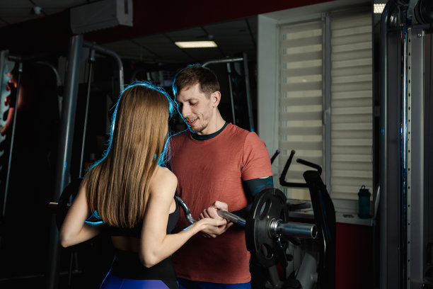 英俊的运动员男子训练二头肌杠铃在健身房与一个女教练的帮助图片下载