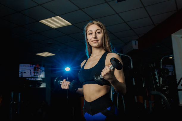 年轻漂亮的女人在健身房用哑铃锻炼。二头肌图片下载