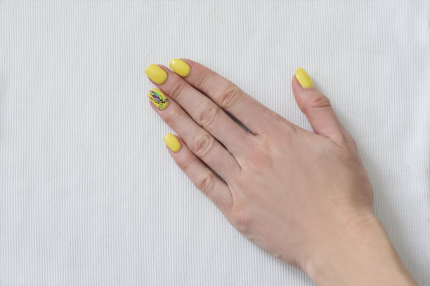 白色织物上有黄色指甲的女性手。关闭了。图片下载