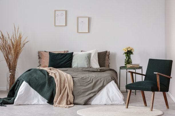 木质扶手椅旁边的床和桌子与花在白色简单的卧室内部。真实的照片图片下载