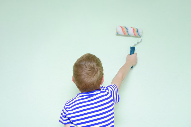 男孩为粉刷墙壁刷墙滚筒。后视图图片下载