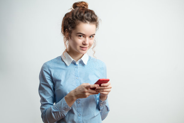 红头发的小学生挽成一个发髻，手里拿着红色的智能手机图片下载