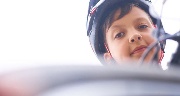 在夏天的一天，十几岁的男孩在公园里戴着保护头盔，坐在他的自行车上，看着摄像机向下看。图片下载