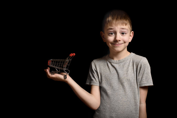 可爱的小男孩手里拿着一个金属购物手推车。孤立在黑色背景上。购物的概念。副本的空间。图片下载