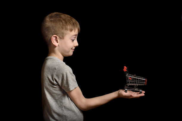 可爱的小男孩手里拿着一个金属购物手推车。孤立在黑色背景上。购物的概念。副本的空间。图片下载
