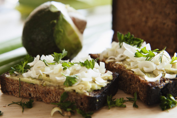 把自制的健康全麦黑麦面包片、鳄梨和洋葱抹在户外桌子上的木砧板上。图片下载