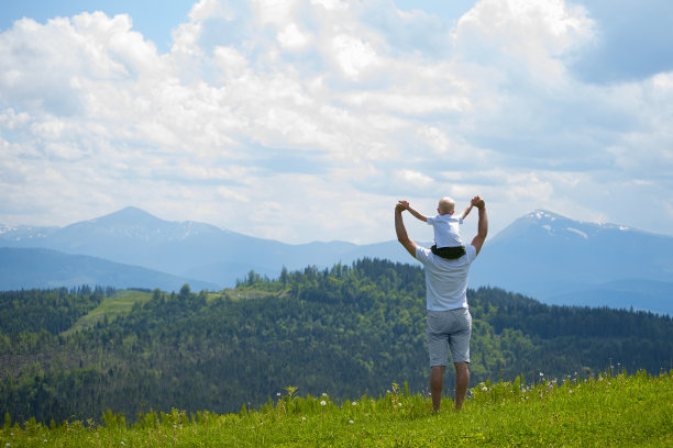 父亲肩上扛着一个小儿子。背景是群山。夏天阳光灿烂的日子。后视图图片下载
