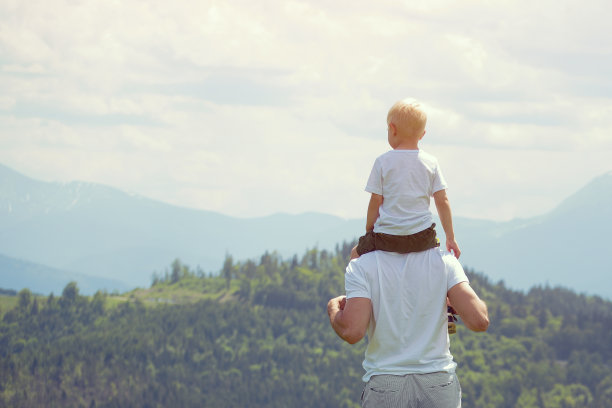 父亲肩上扛着一个小儿子。背景是群山。夏天阳光灿烂的日子。后视图图片下载