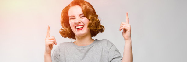 灰色背景上穿着灰色t恤的迷人年轻女孩。女孩手指向上图片下载