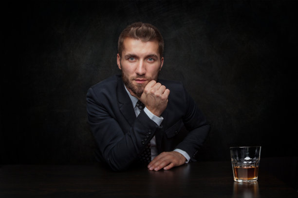 有魅力的商人拿着一杯威士忌，背景是黑色图片下载