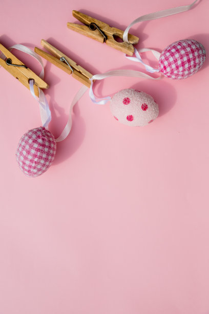 五彩缤纷的复活节彩蛋与十字架挂在晾衣夹的线。静物复活节彩蛋挂在一根绳子上，粉红色的背景。复活节假期的概念。本空间图片下载